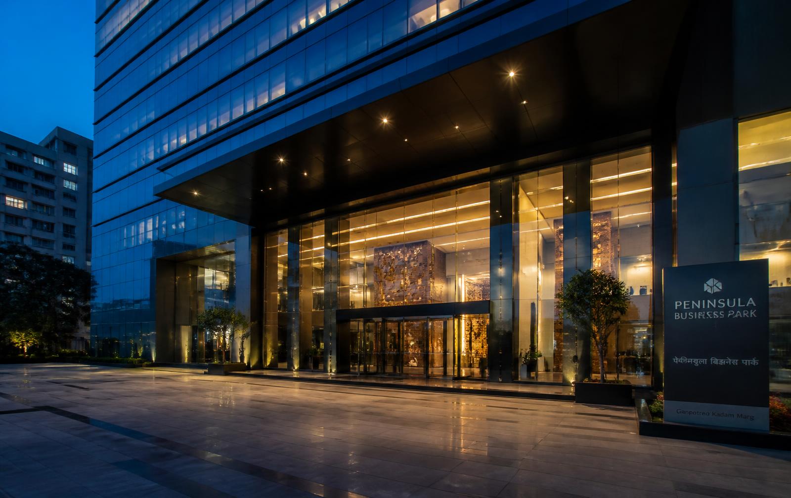 Glass corporate office tower entrance lit at blue hour